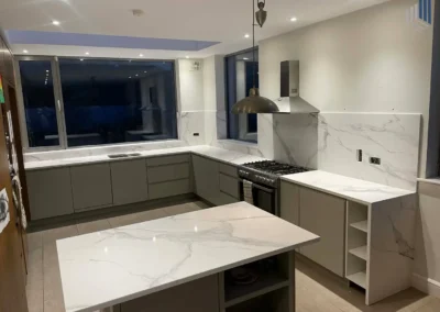 Modern L-shaped kitchen with marble countertops, grey cabinets, and a stainless steel range hood over a gas stove.]>>